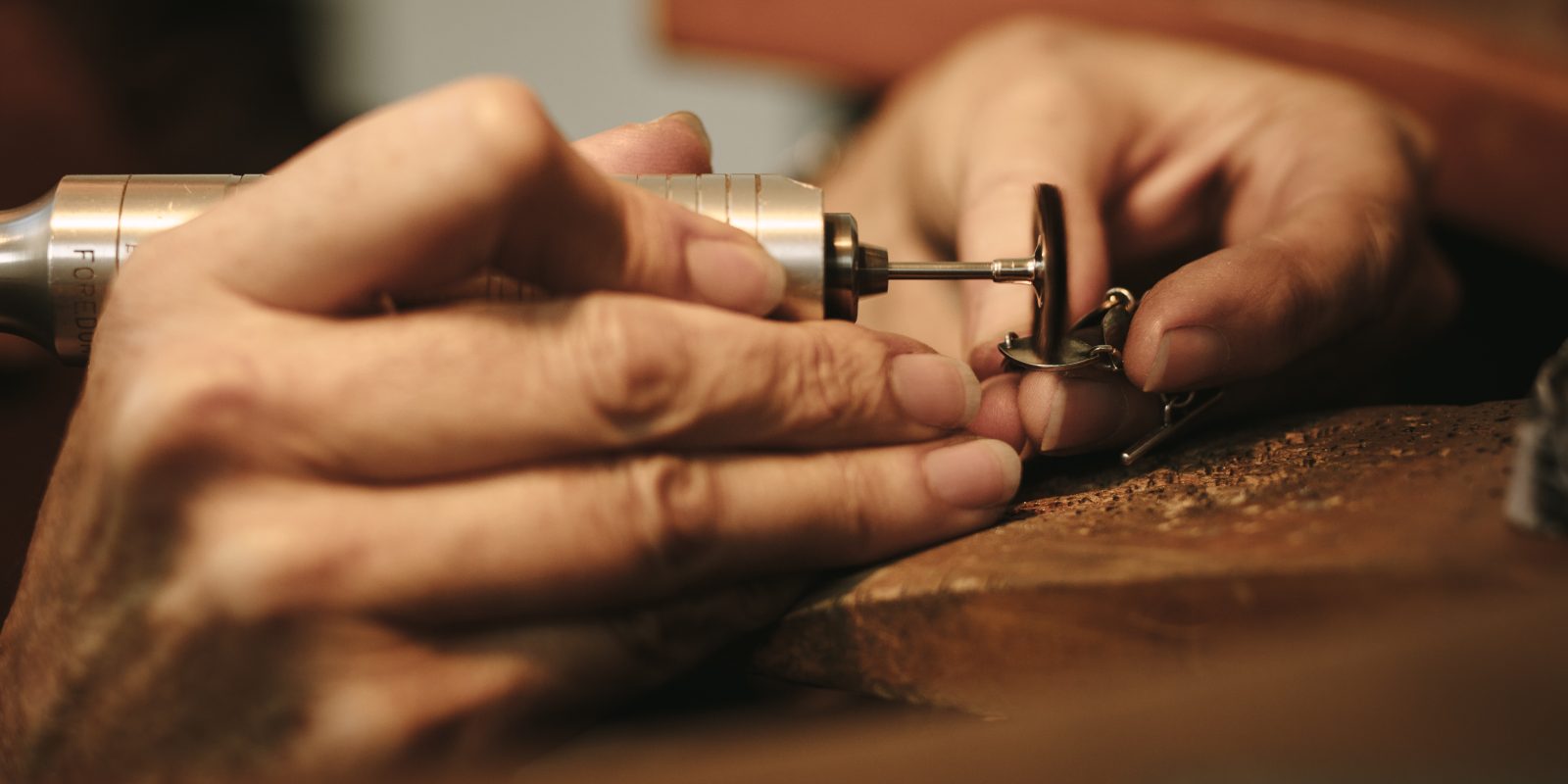 Hands of jeweler polishing a jewelry piece with flex shaft.